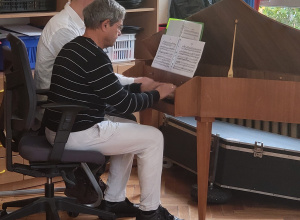 Dwóch muzyków grających na klawesynie; instrument z nutami ustawiony w sali, podczas zajęć muzycznych dla dzieci.