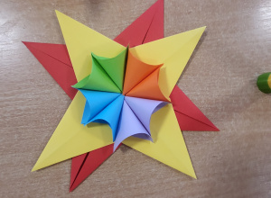 Dzieci wykonujące papierowe, kolorowe gwiazdy świąteczne podczas zajęć plastycznych, przy stolikach w sali.